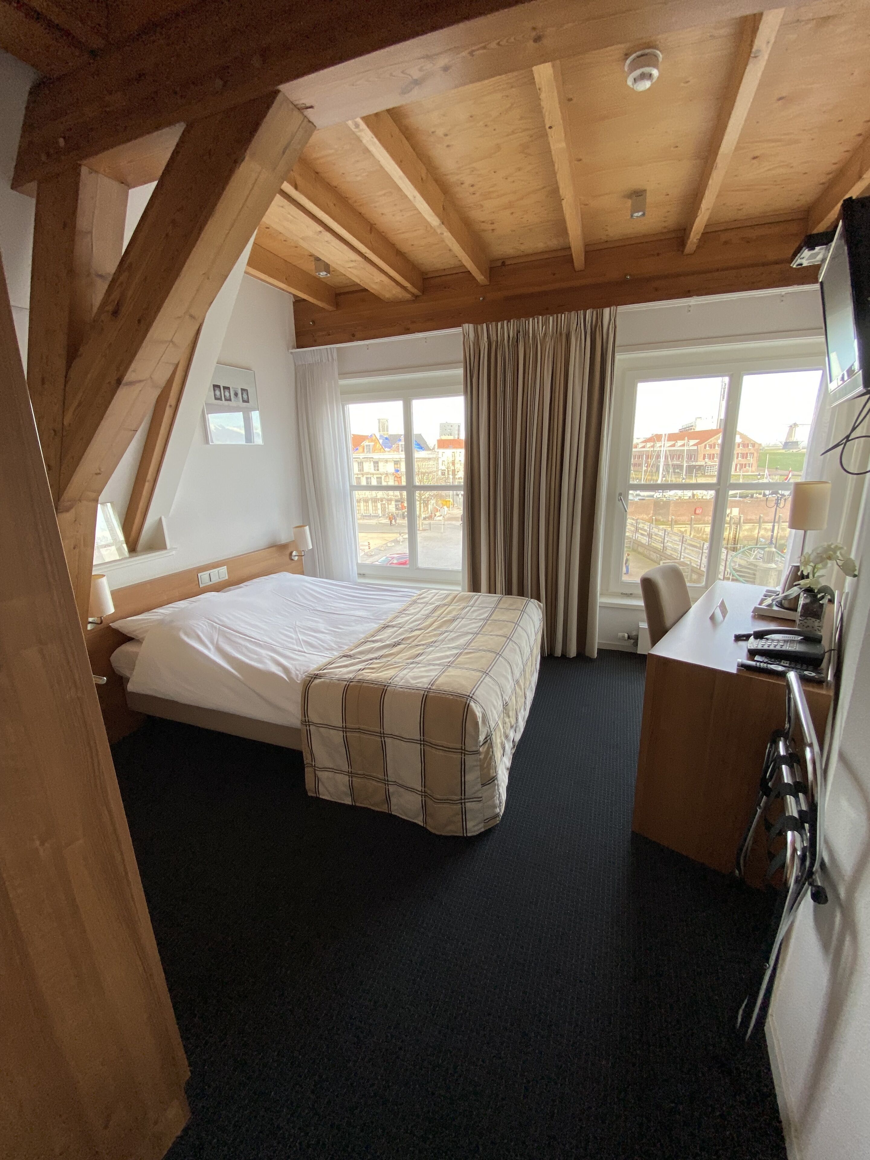 Une chambre avec un lit, un bureau et une fenêtre avec des rideaux.