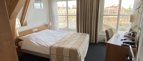 A room with a bed, a desk, and a window with curtains.