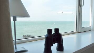 A window with binoculars on a windowsill, a lamp, and a view of the sea.