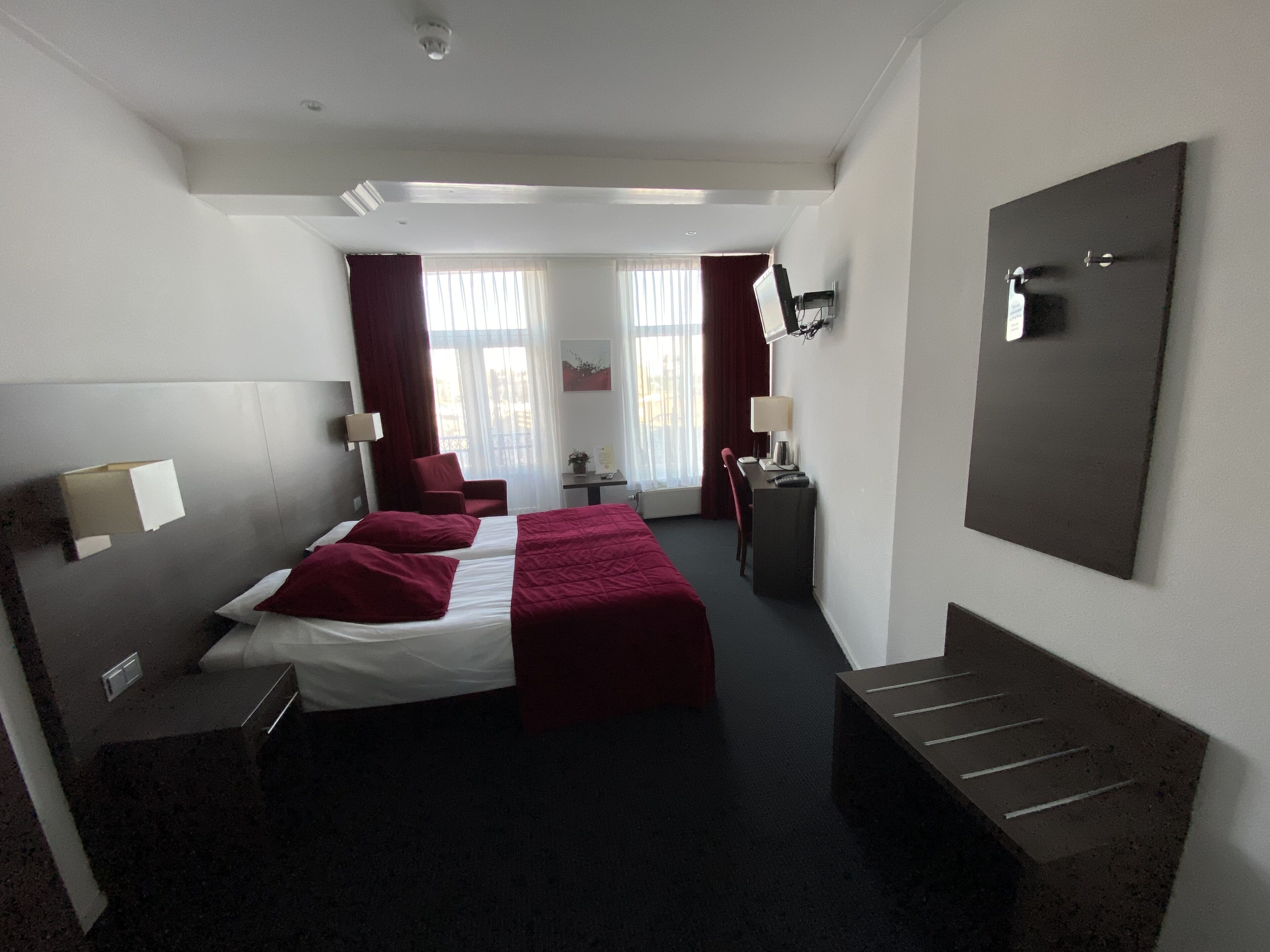Een hotelkamer met twee bedden, een bureau, een stoel, een televisie en een grote spiegel.
