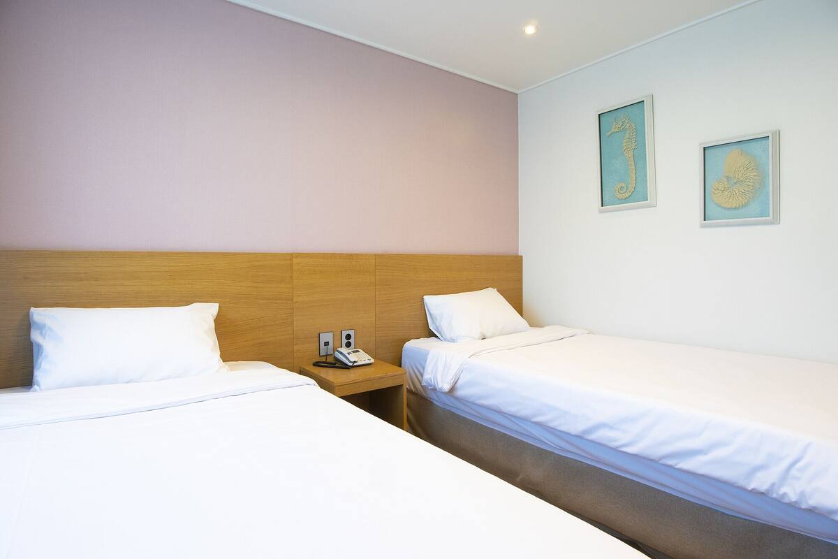 A hotel room with two single beds, a wooden headboard, a bedside table with a phone and a lamp, and two framed seahorse artworks on the wall.