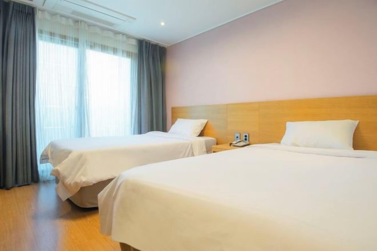 A hotel room with two beds, a wooden headboard, a telephone, and a window with curtains.