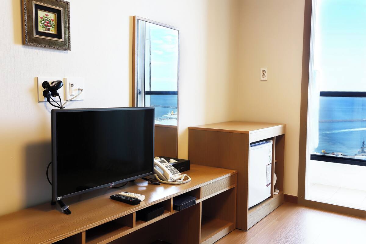 A hotel room with a TV, phone, and a small desk.