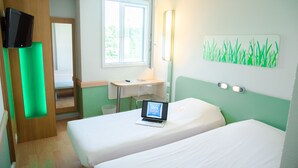 A hotel room with two beds, a desk with a laptop, a TV, and a window with a view of greenery. - ibis budget Aeroport le Bourget Garonor (Le Blanc-Mesnil)