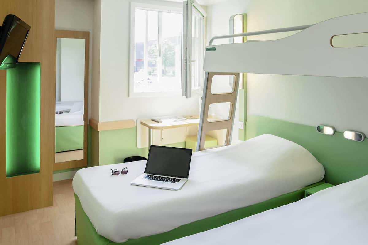A bunk bed room with a laptop on the lower bunk, a desk, and a window.