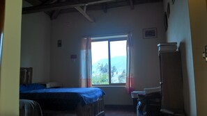 Quarto com duas camas, janela com cortinas, guarda-roupa de madeira e vista para o verde lá fora.