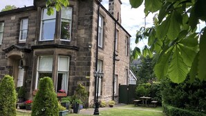 A stone building with a traditional design, featuring a well-maintained garden with various plants and a small outdoor seating area. - The Alba House (Edinburgh)