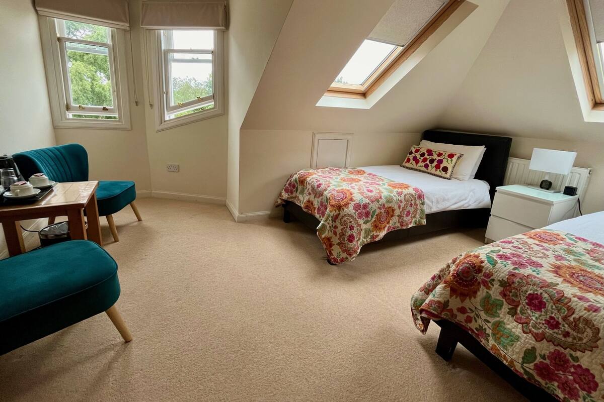 A bedroom with two beds, a desk, and a chair. There are windows and a skylight.