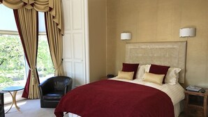 A hotel room with a large bed, a nightstand, a chair, and a view of greenery outside. - The Alba House (Edinburgh)