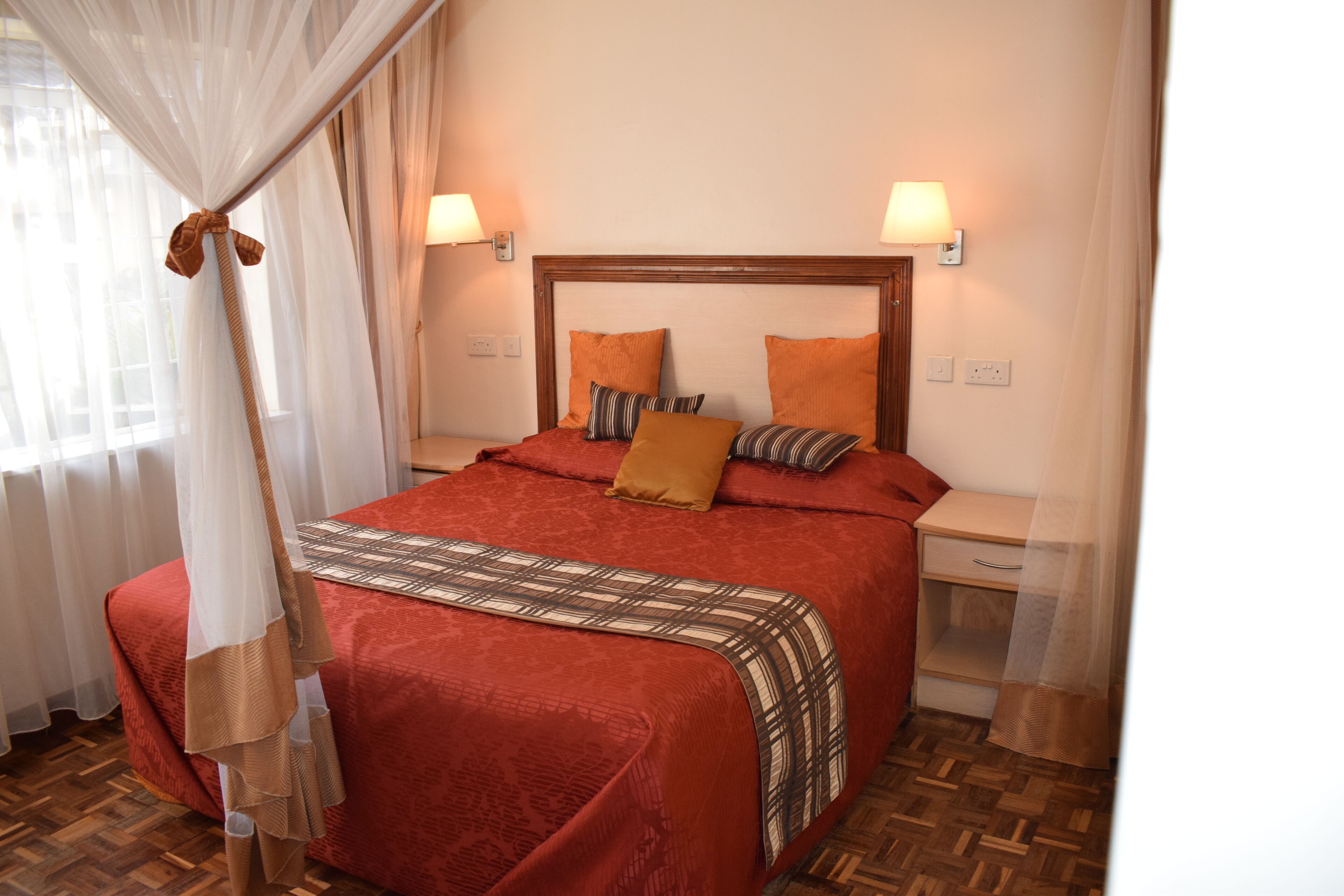 Ein ordentlich bezogenes Bett mit roter Tagesdecke, zwei Kissen und einem Baldachin.