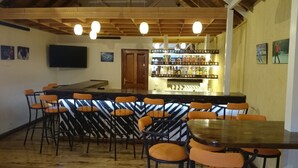 Een bar met houten plafond, barstoelen en een toonbank vol flessen.