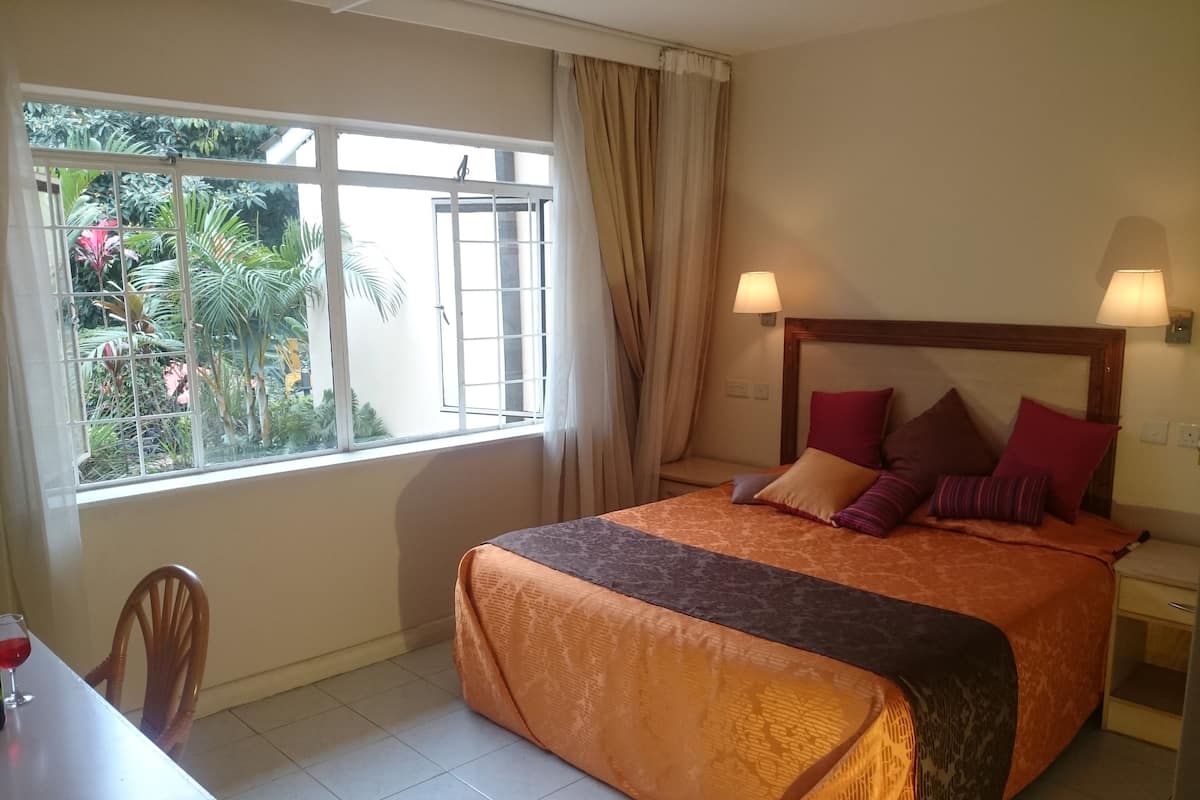 A hotel room with a bed, a window with curtains, a table with a glass of red wine, and a chair.