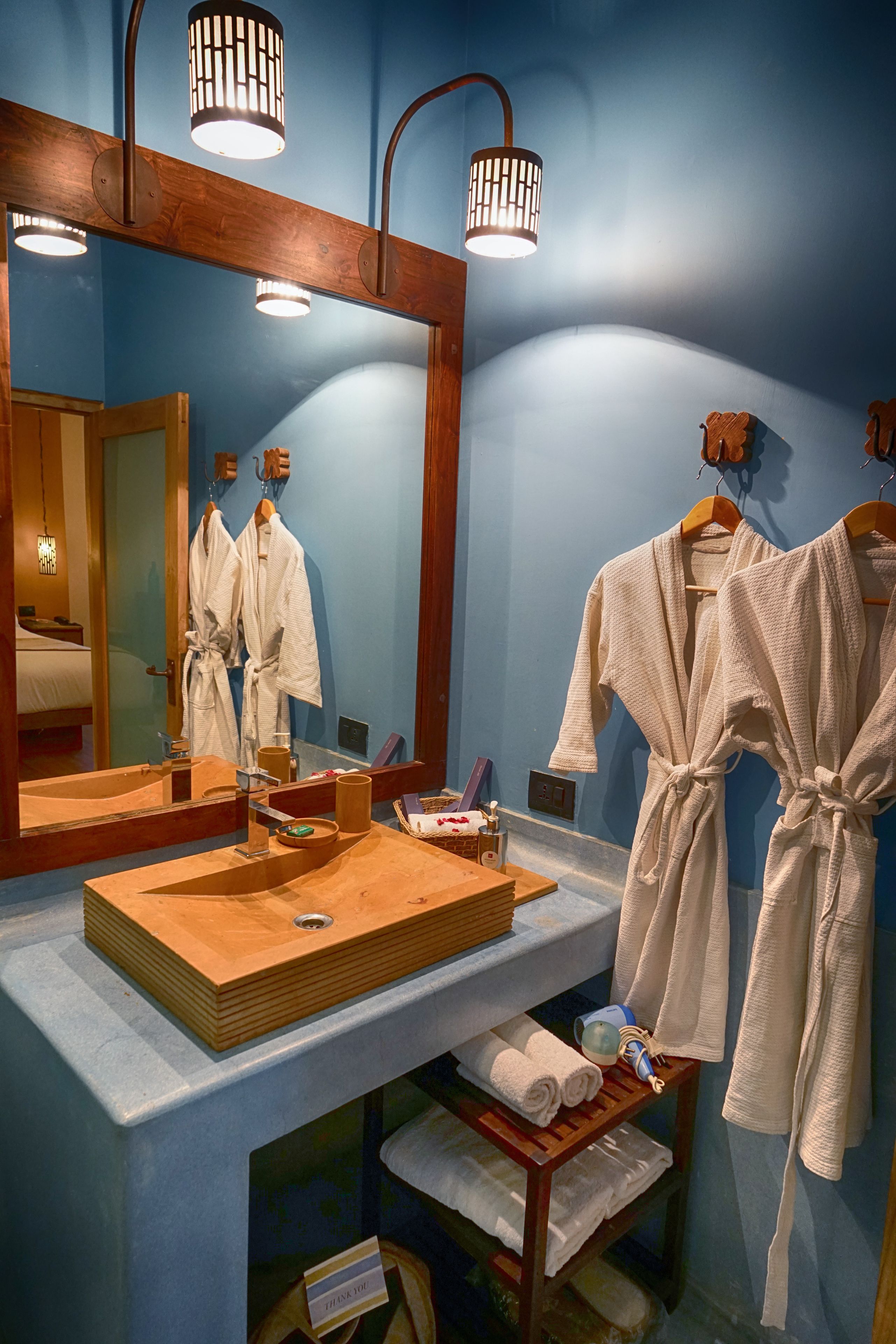 A bathroom with a large mirror, wooden vanity, and two white bathrobes hanging on the wall.