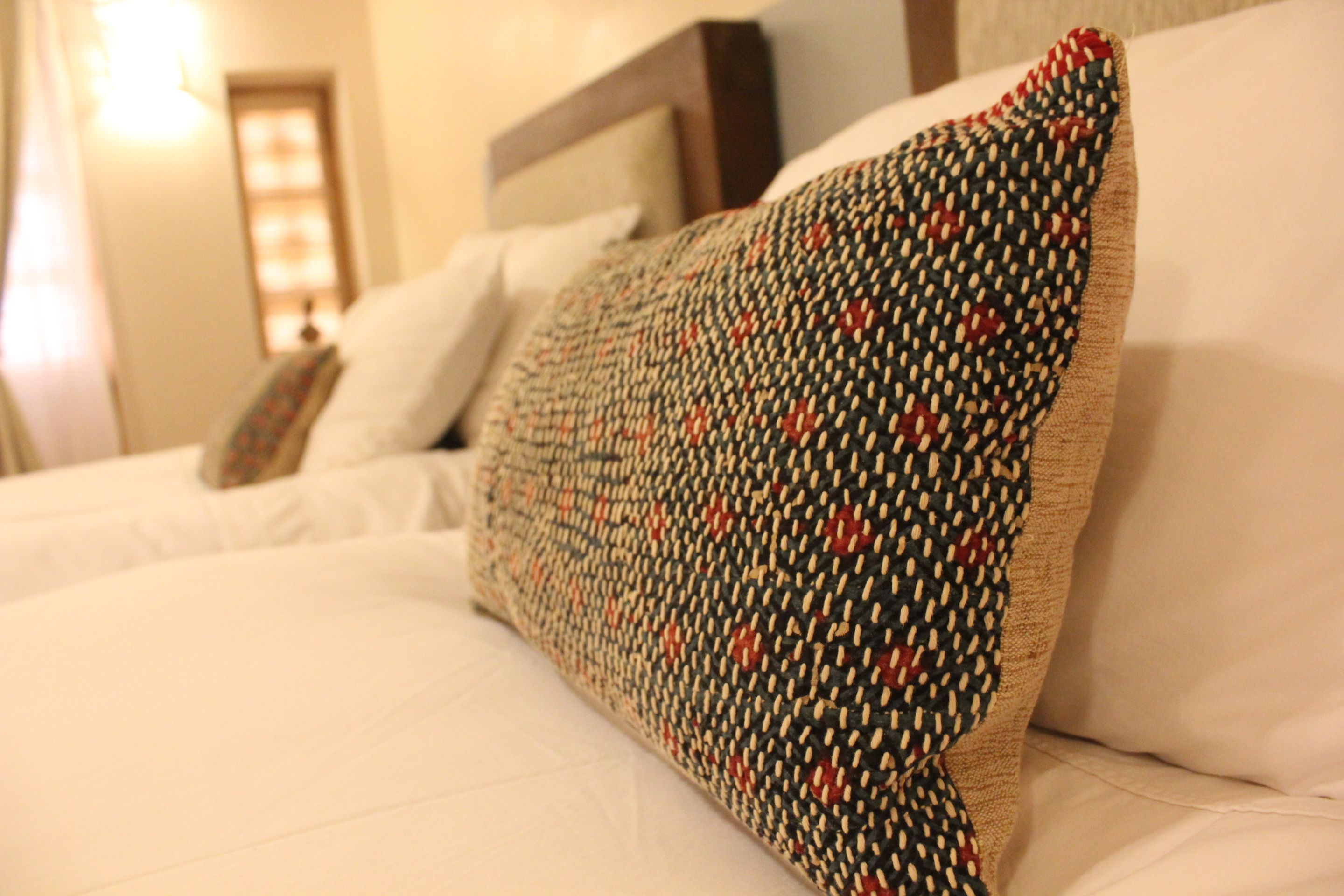 A bed with white linens and a patterned pillow.