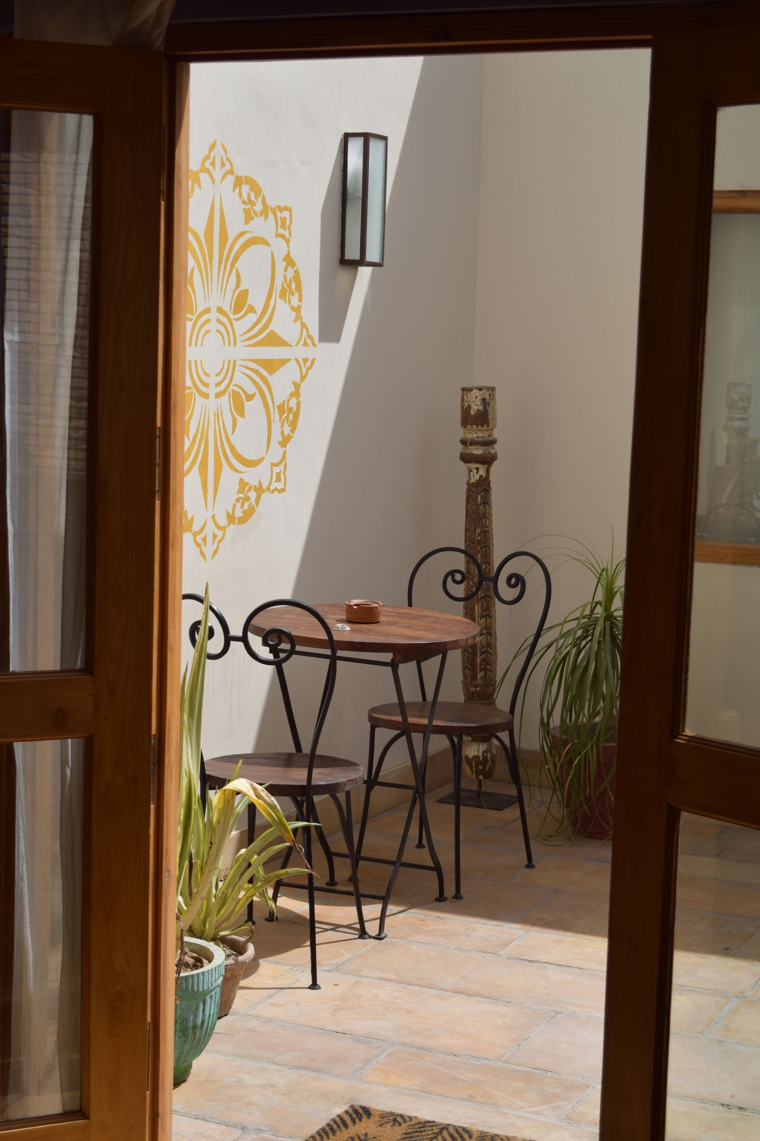 A patio with a wooden table and chairs, a potted plant, and a decorative wall.