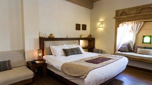 A neatly arranged bedroom with a large bed, a bedside table, a chair, and a window with curtains. - 1st Gate Home - Fusion (Jaisalmer)