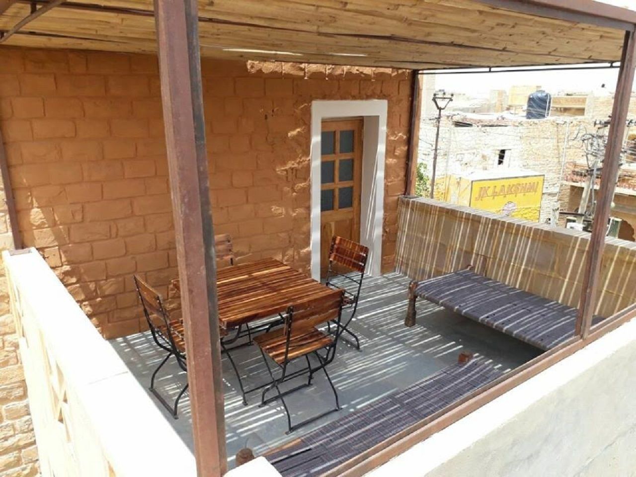 A covered outdoor area with a brick wall, a wooden table with metal chairs, a bench, and a door.