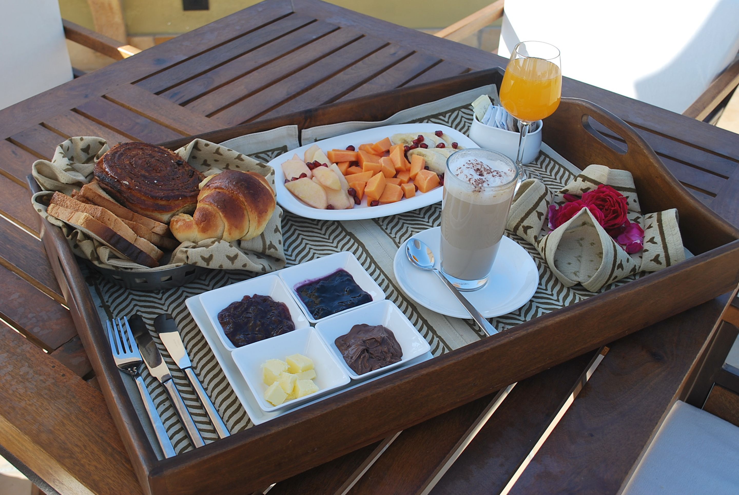 A tray with food items including bread, fruits, and a drink on a wooden table.
