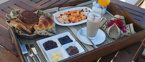 A tray with food items including bread, fruits, and a drink on a wooden table.