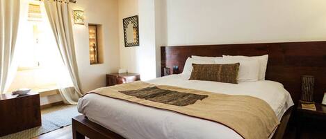 A neatly arranged bedroom with a large bed, a bedside table, a nightstand, and a window with curtains.