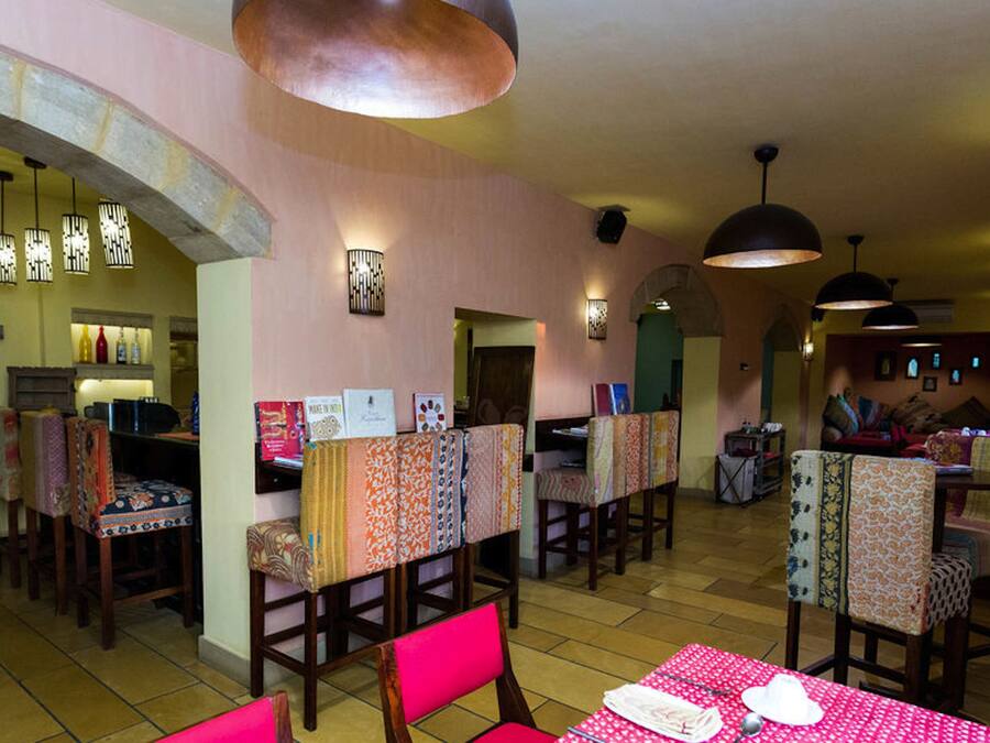 A restaurant with booths and tables, featuring patterned tablecloths and chairs, and pendant lighting.