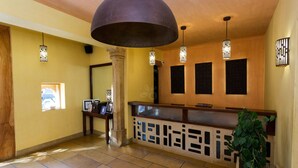 A reception area with a wooden reception desk, a large pendant light, and wall-mounted lights. - 1st Gate Home - Fusion (Jaisalmer)