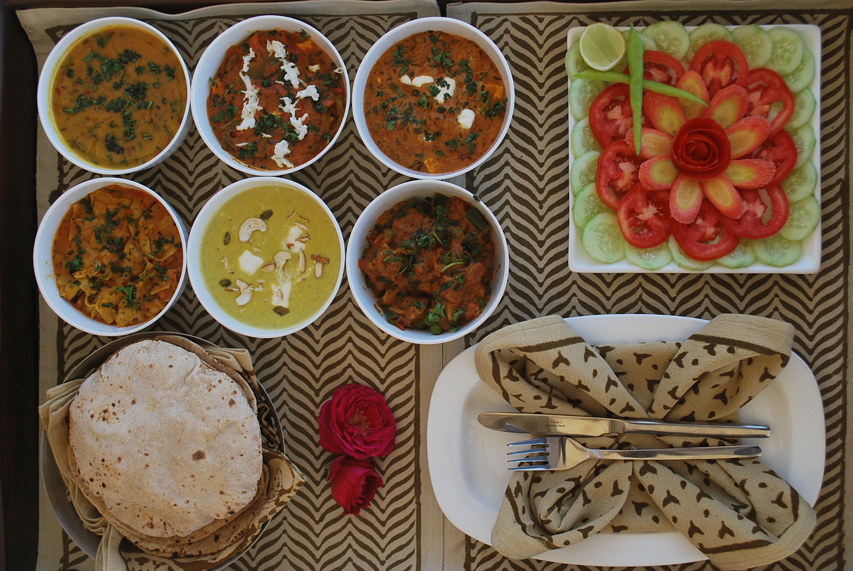 Una mesa con diversos platos, incluyendo cuencos de curry, una fuente de tomates en rodajas y panes planos.