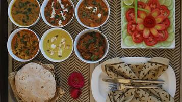 Una mesa con diversos platos, incluyendo cuencos de curry, una fuente de tomates en rodajas y panes planos.