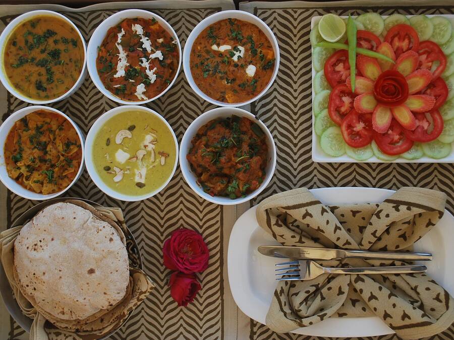 Una mesa con diversos platos, incluyendo cuencos de curry, una fuente de tomates en rodajas y panes planos.