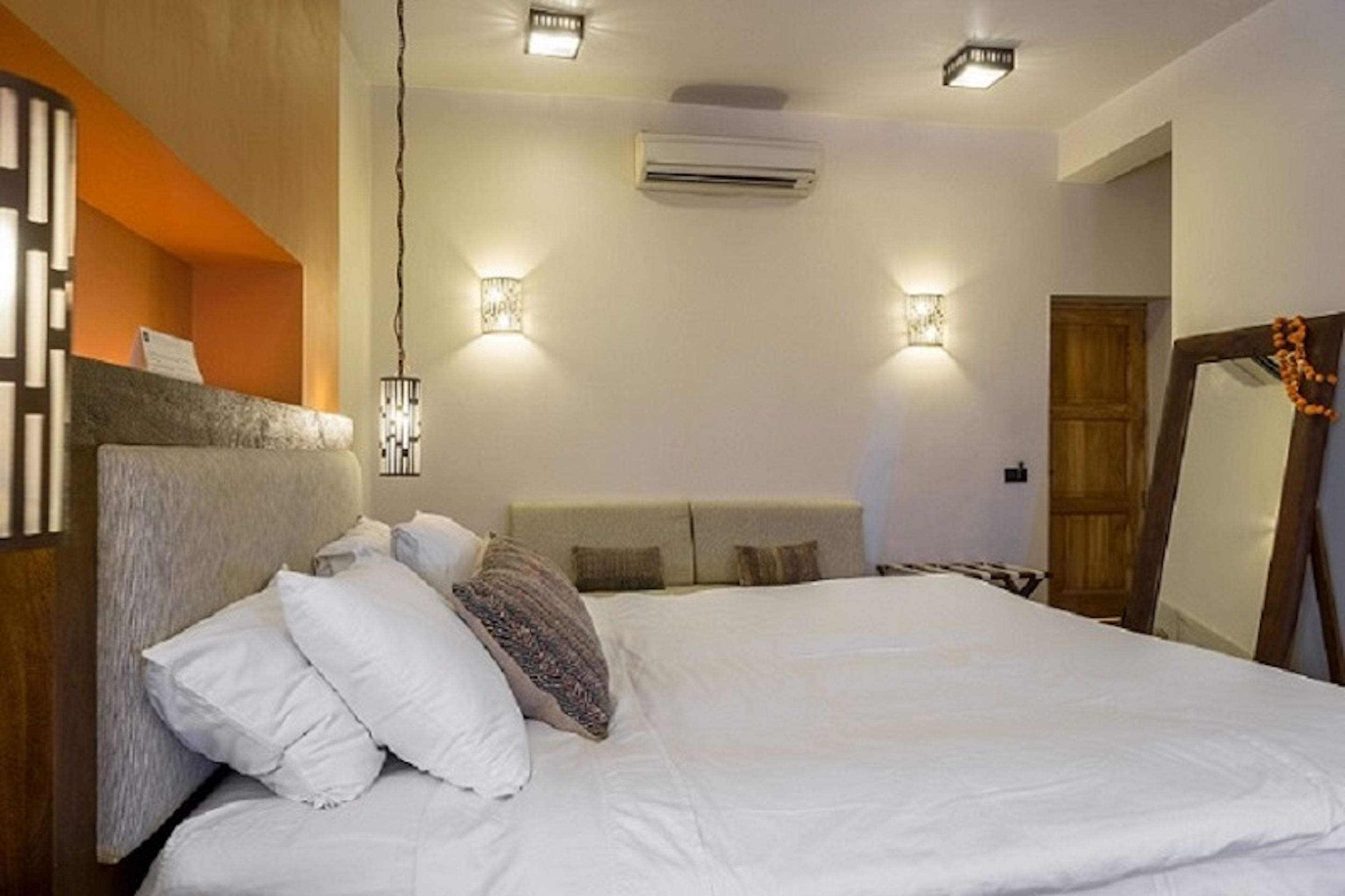 Une chambre à coucher avec un lit, deux lampes fixées au mur, un climatiseur et une porte en bois.