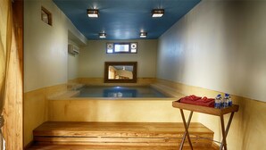 A sauna room with wooden flooring, a wooden bench, a table with towels and bottles, and a ceiling with recessed lighting. - 1st Gate Home - Fusion (Jaisalmer)