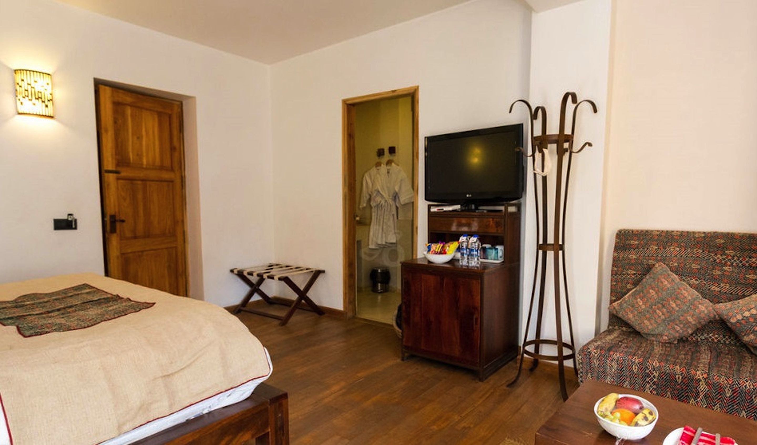 A hotel room with a bed, a TV, a wooden cabinet, a sofa, and a small table with a bowl of fruit.