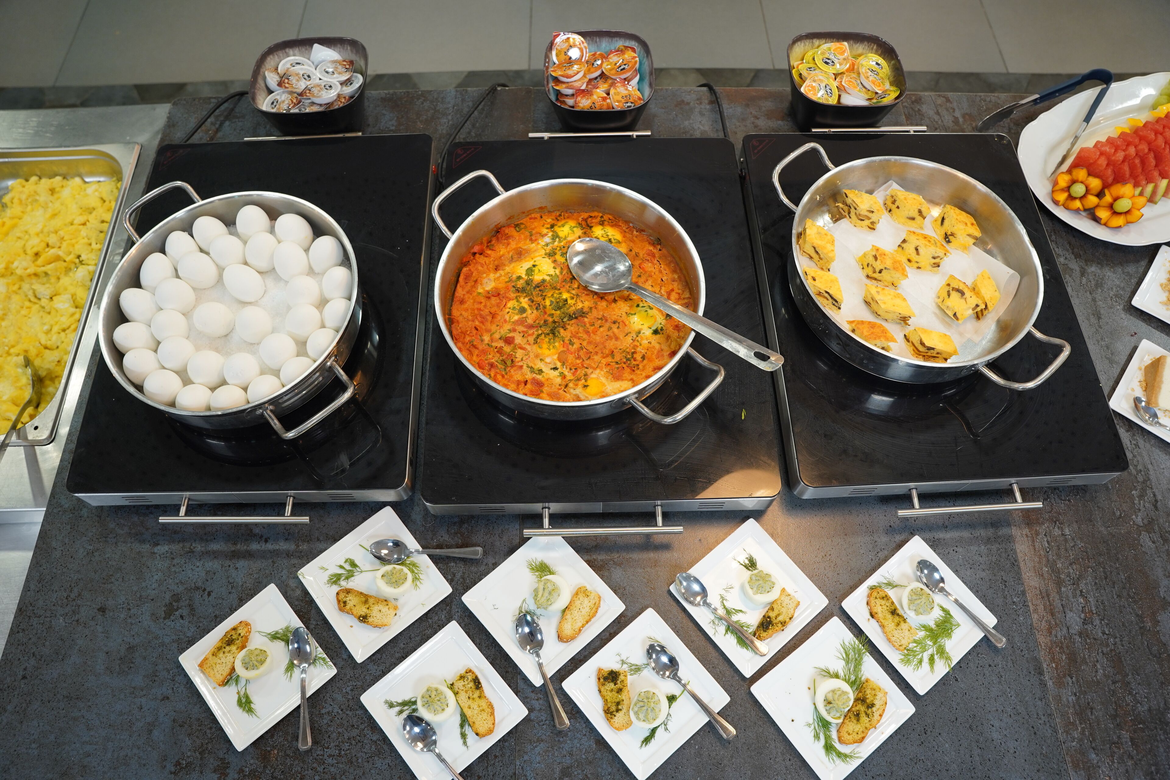 Montaje de bufé con diversos platos, incluyendo huevos, un guiso de tomate y mariscos.
