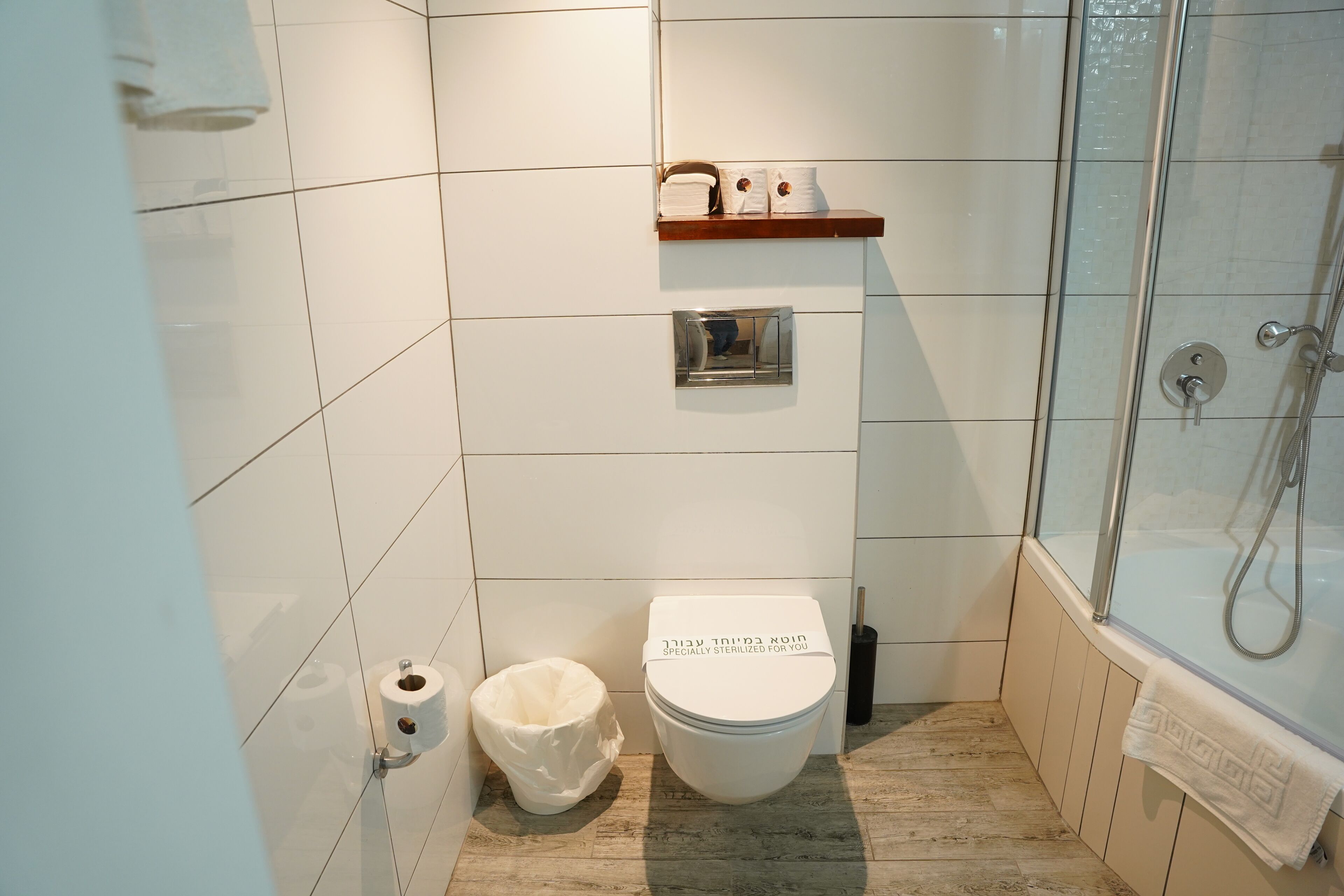 A bathroom with a toilet, a shower, and a shelf with toiletries.