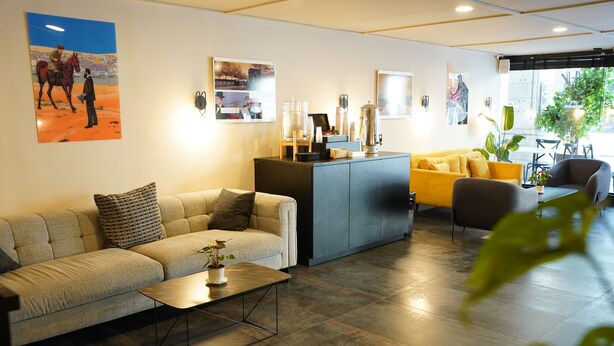 A modern hotel lobby with a sofa, a coffee table, a reception desk, and a yellow armchair. - Spirit of Herzl Hotel (Jerusalem)