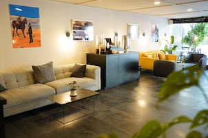 Un moderno hall de hotel con un sofá, una mesa de centro, un mostrador de recepción y un sillón amarillo.