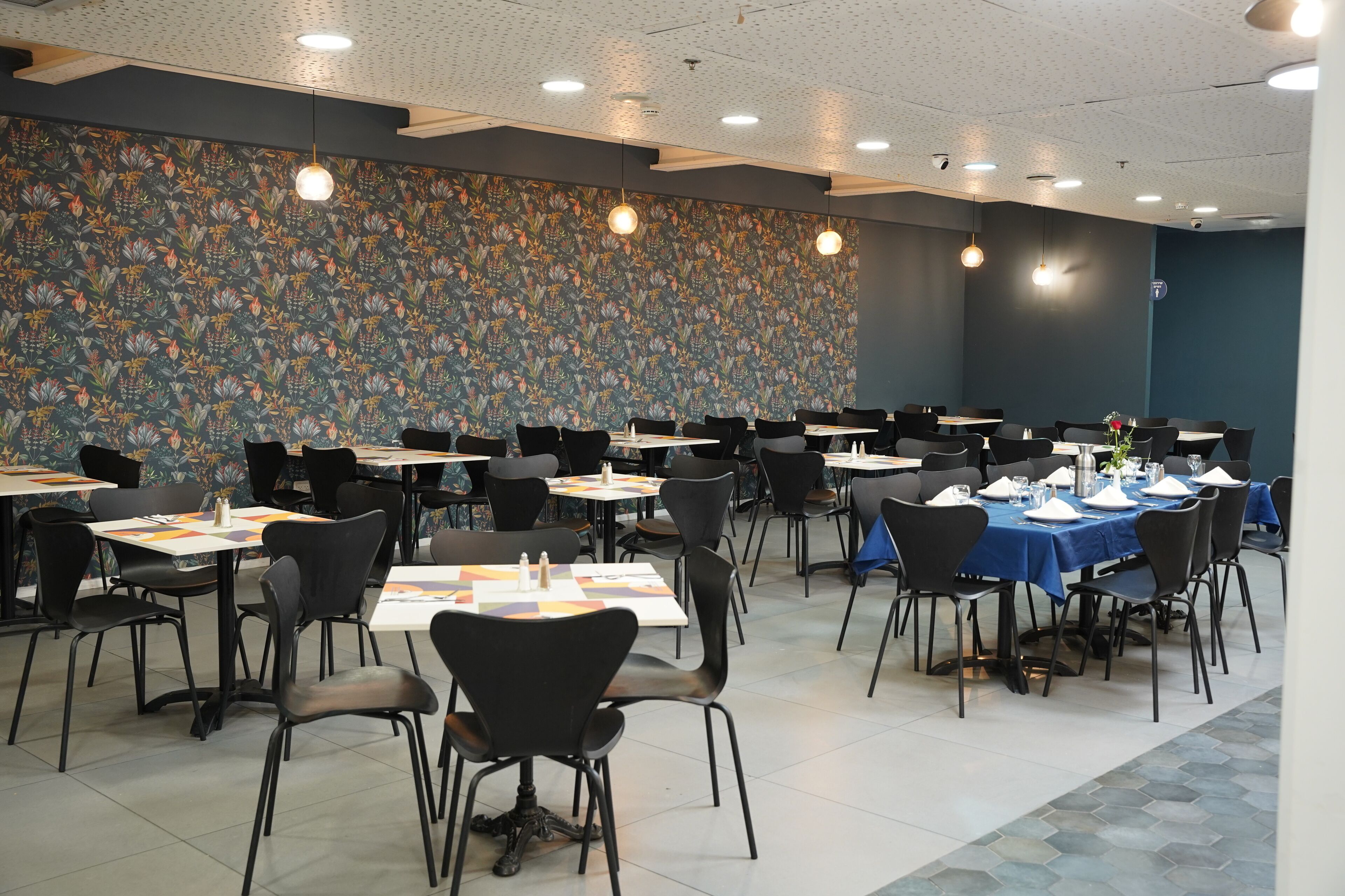 Un salón de conferencias con varias mesas y sillas, un papel tapiz decorativo y luces en el techo.