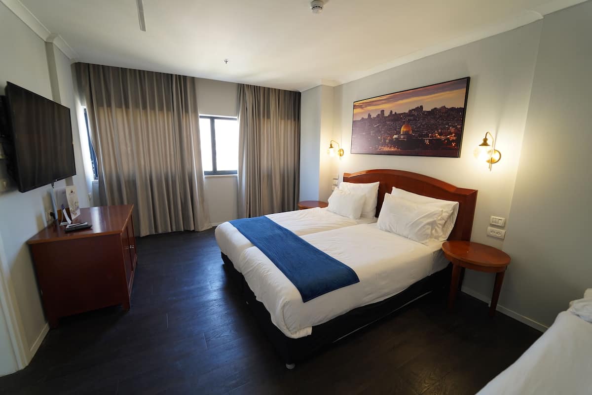 Une chambre d’hôtel avec un grand lit, un téléviseur à écran plat, une table de chevet en bois, un bureau et un tableau représentant un paysage urbain.