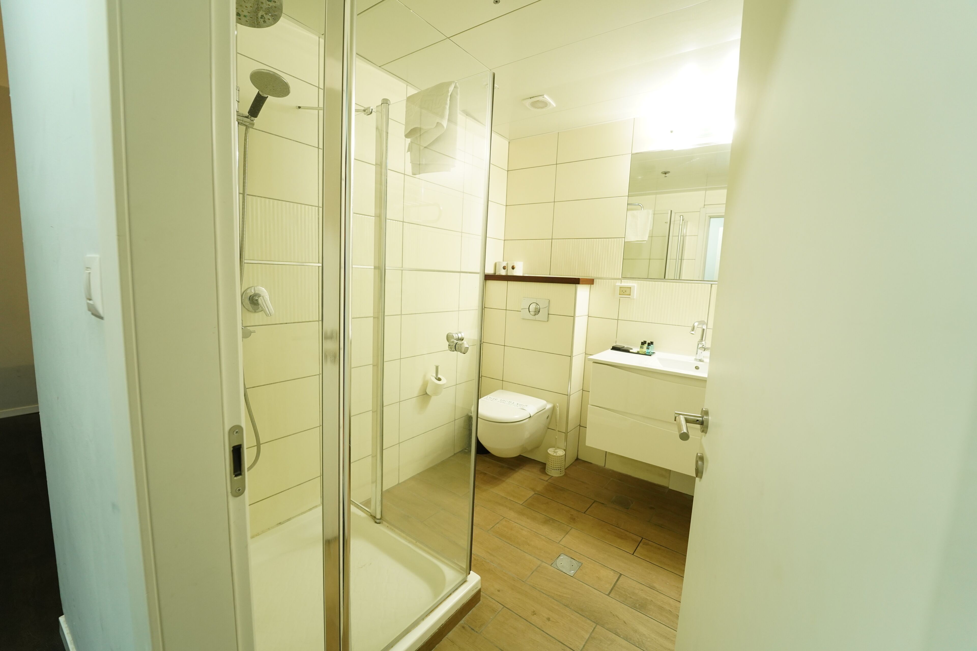 A bathroom with a glass-enclosed shower, a toilet, and a sink with a mirror above it.