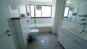Een moderne badkamer met witte tegels, een badkuip, toilet, wastafel en een grote spiegel.