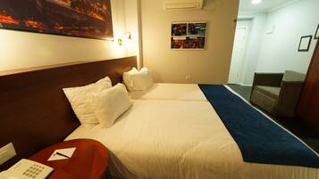 Una habitación de hotel con una cama grande, una mesita de noche con teléfono, aire acondicionado en la pared y un cartel en la pared.
