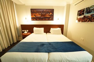 Habitación de hotel con dos camas, vistas a la ciudad, una mesita de noche con un teléfono y un cuadro colgado en la pared.