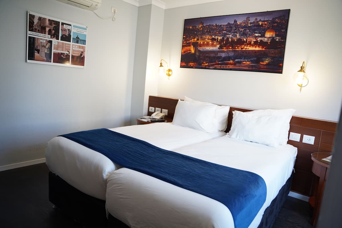 Une chambre d’hôtel avec un grand lit, un tableau représentant un paysage urbain accroché au mur et une table de chevet avec une lampe.