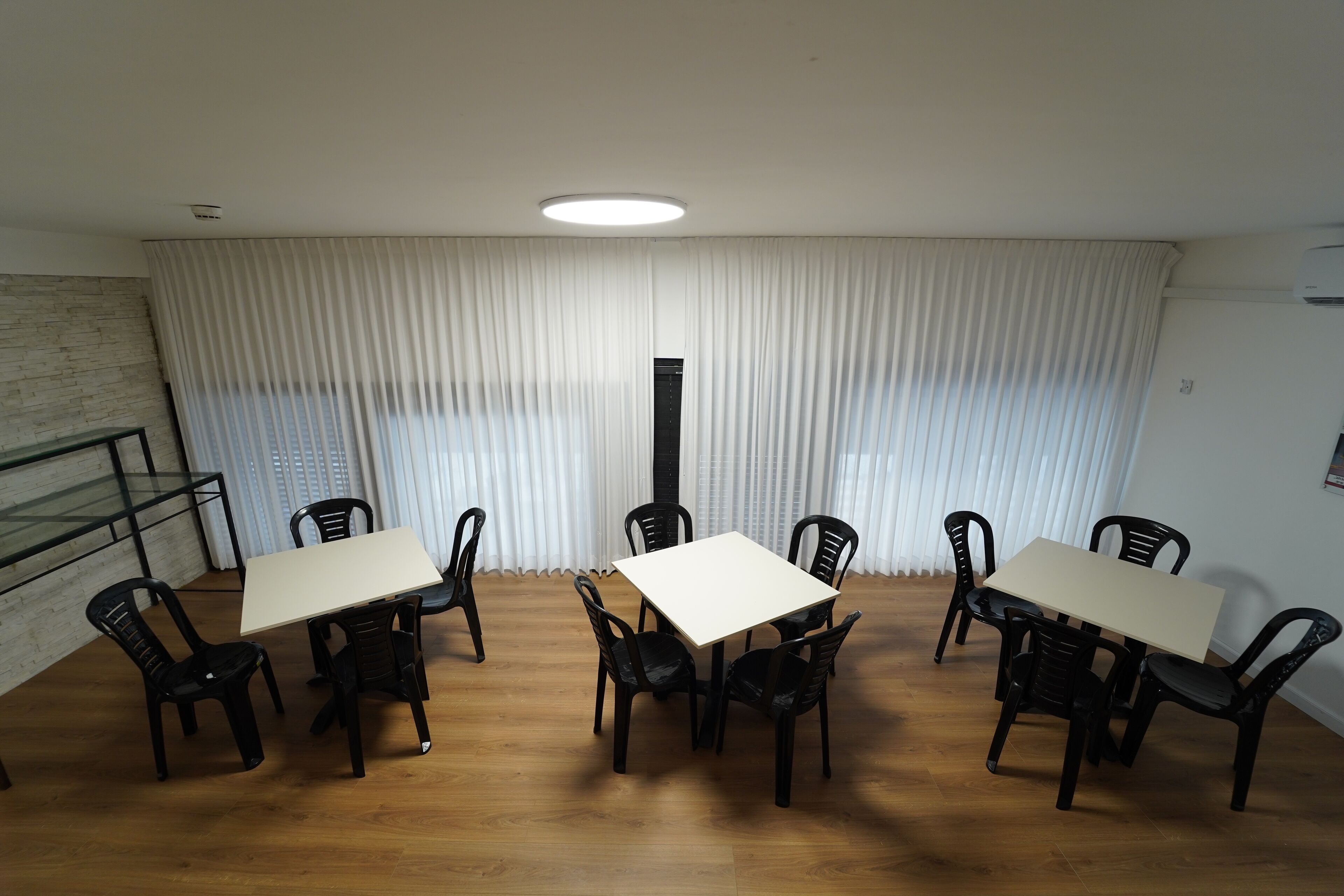 A conference room with a white table and black chairs, a wooden floor, and a large window with white curtains.
