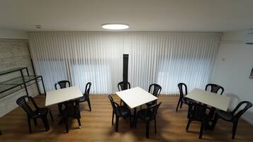 A conference room with a white table and black chairs, a wooden floor, and a large window with white curtains.