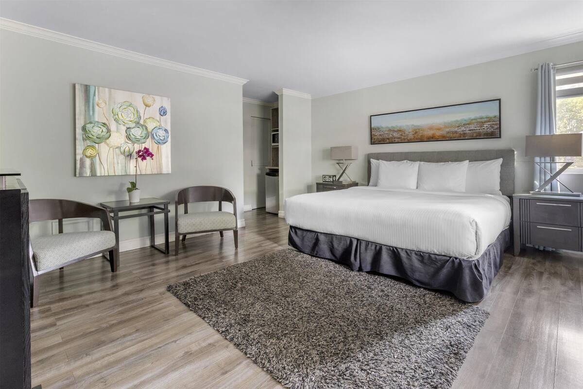 A modern hotel room with a large bed, a desk, a chair, and a painting on the wall.