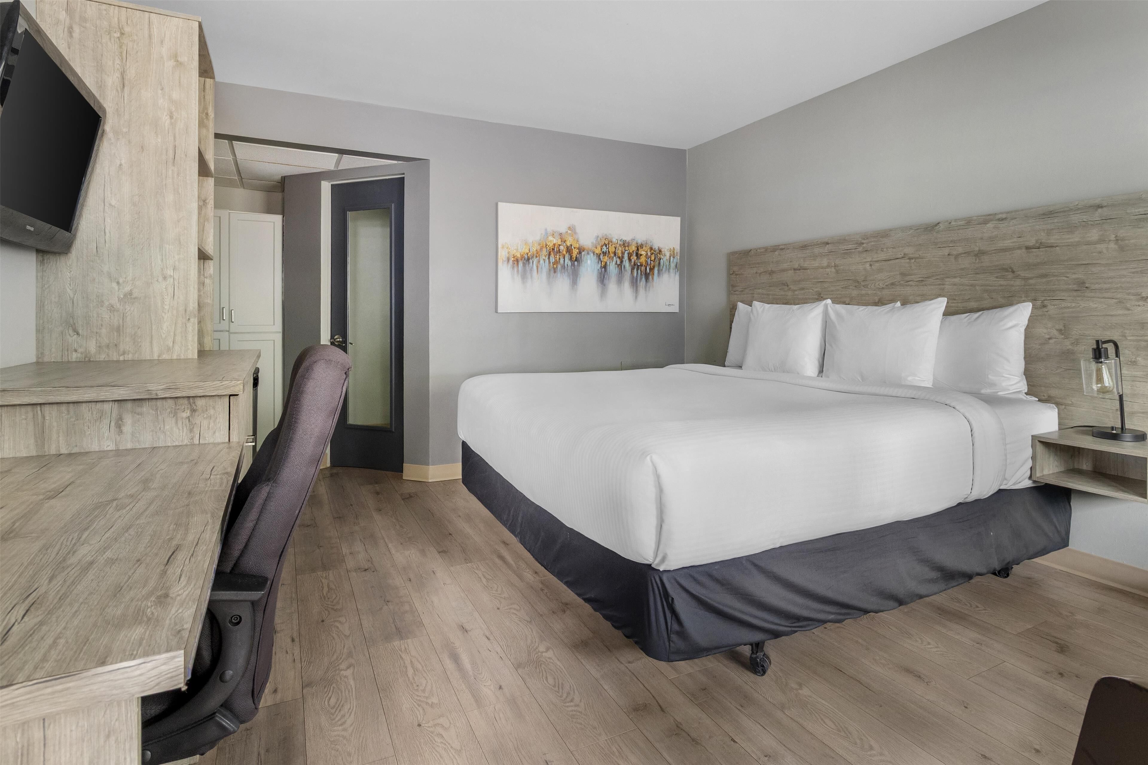 Ein modernes Hotelzimmer mit Schreibtisch aus Holz, einem bequemen Sessel, einem großen Bett und einem Gemälde an der Wand.