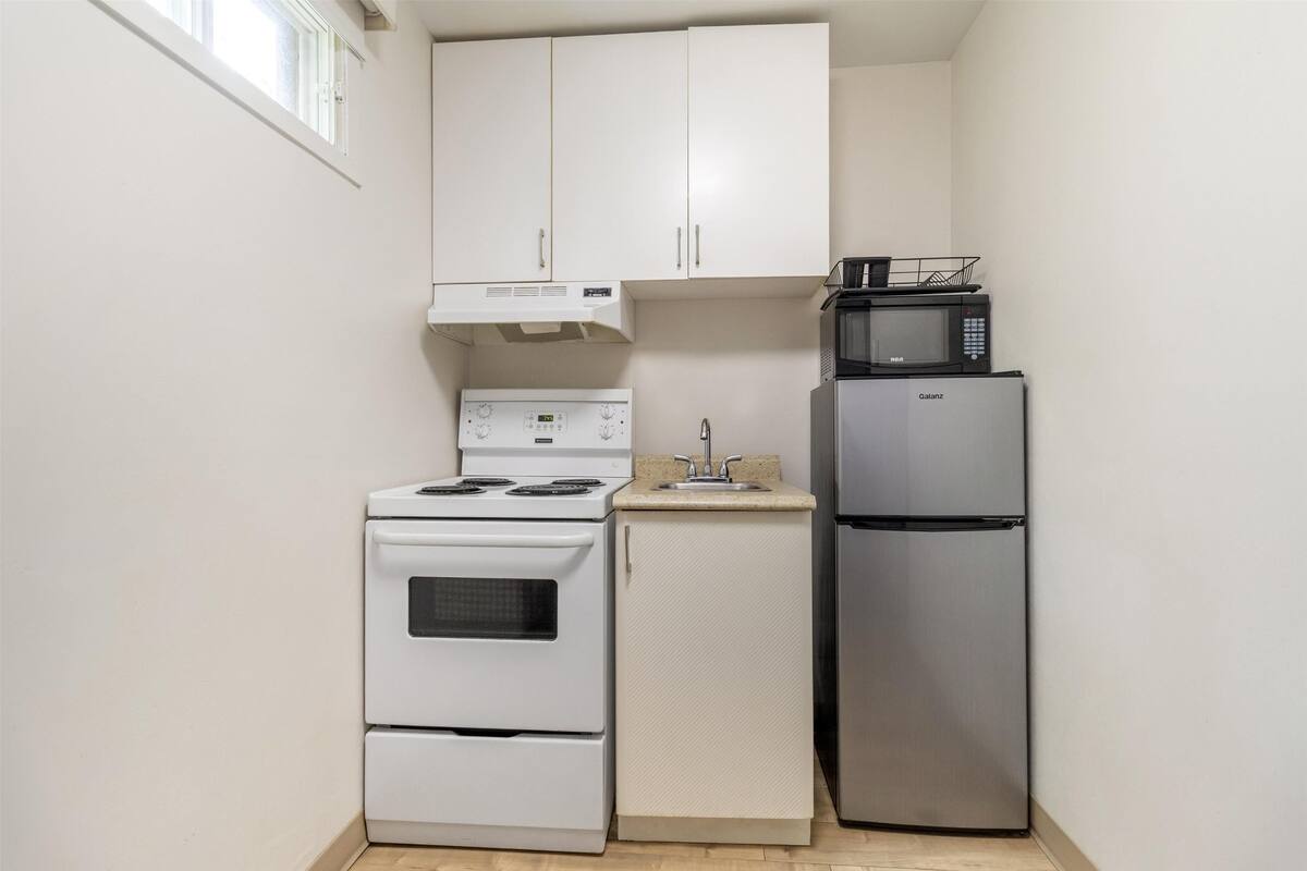 A compact kitchen with white cabinets, a stove, a microwave, and a refrigerator.