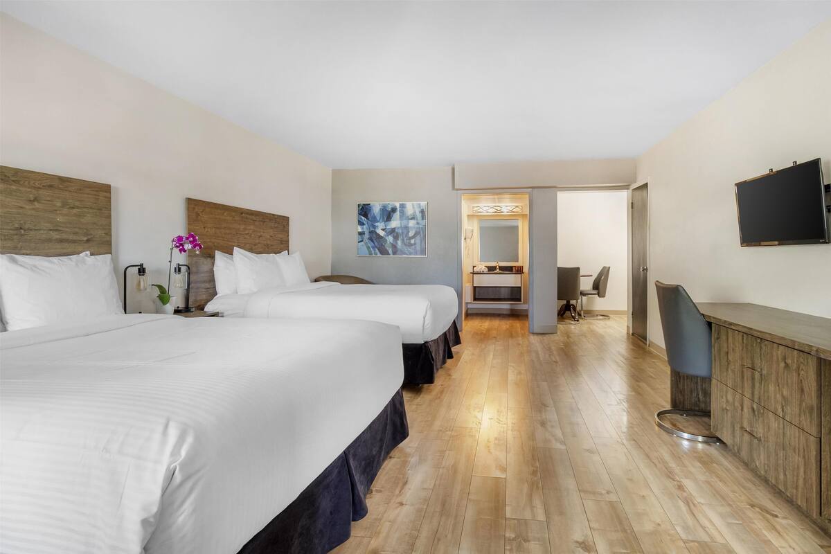 A hotel room with two beds, a wooden headboard, a flat-screen TV, a desk, and a chair.