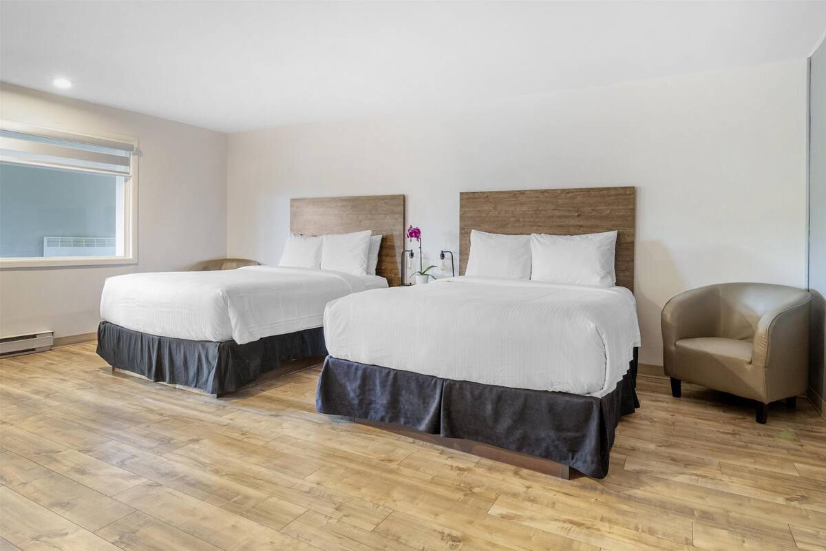A hotel room with two beds, a chair, and a window.
